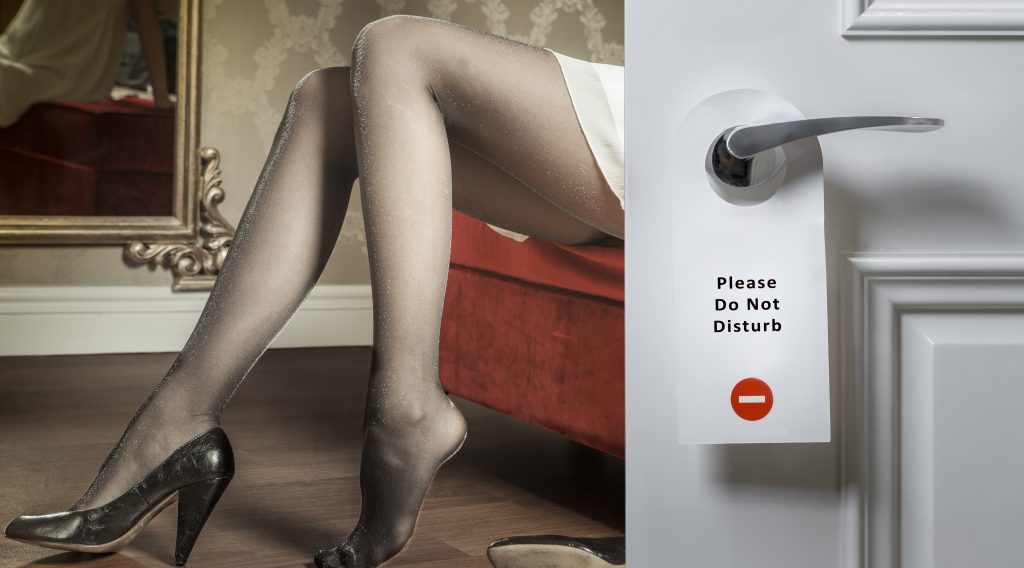 Image of woman sitting on a chair wearing panty hose behind a door with a "Please do not disturb" sign on it